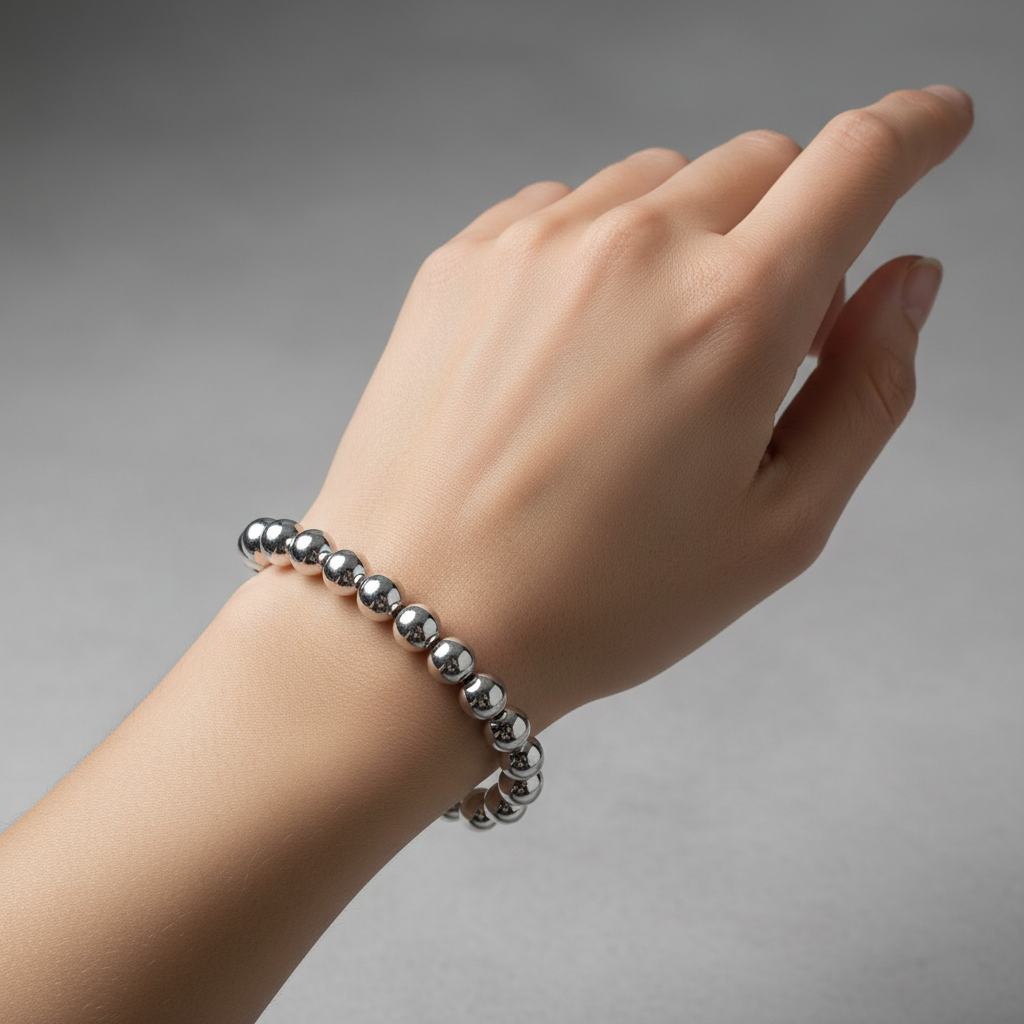 Hand model wearing a silver beaded bracelet on a gray background